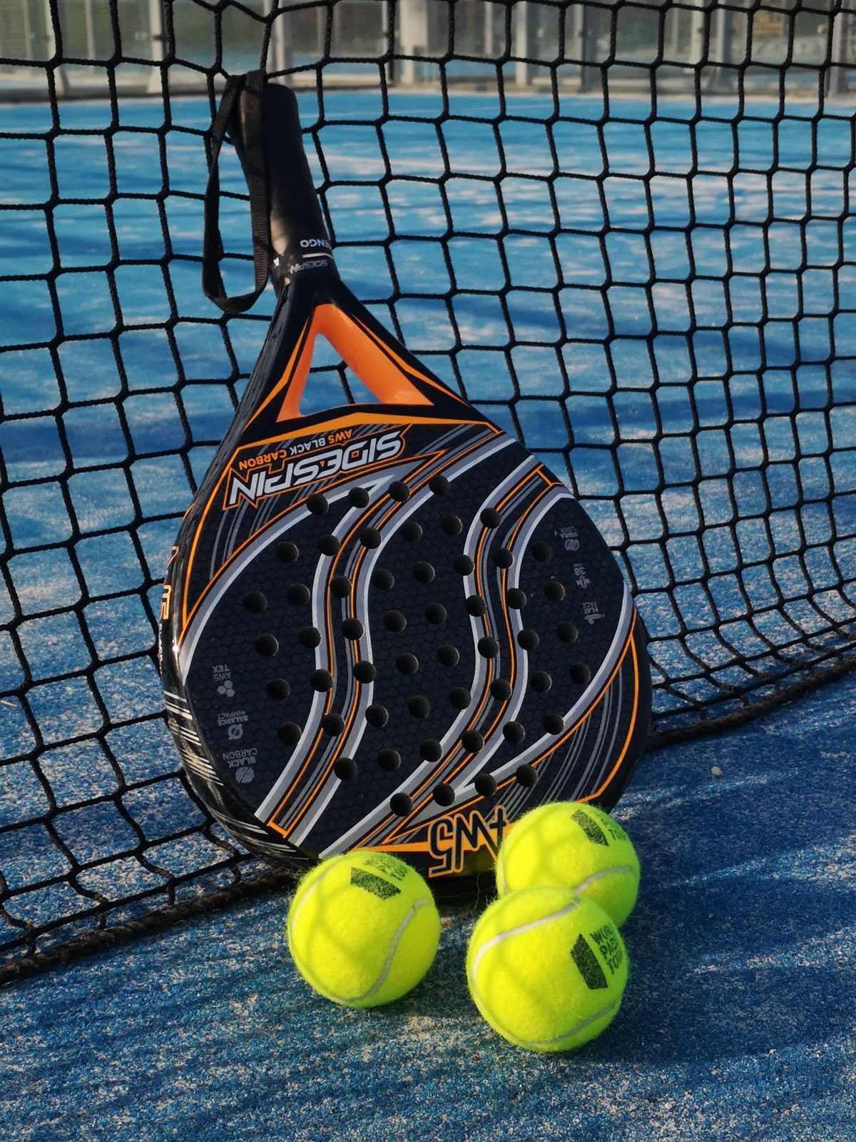 Padel racket leaning against a net with yellow balls