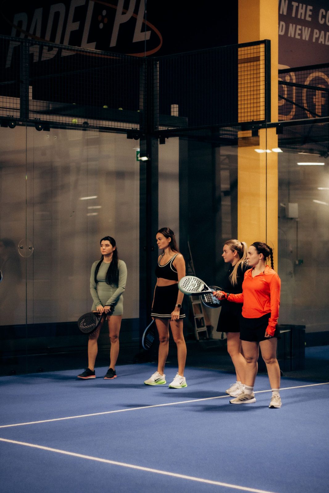 Four players in a doubles padel match on an indoor court