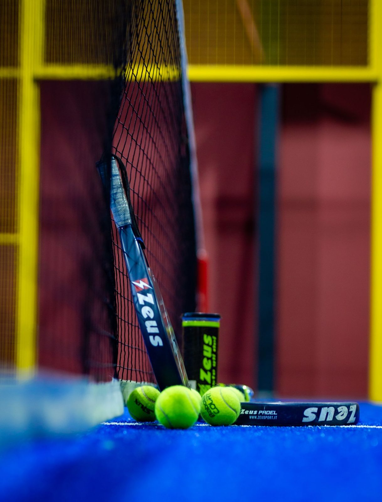 Padel racket and balls by the net on an indoor court