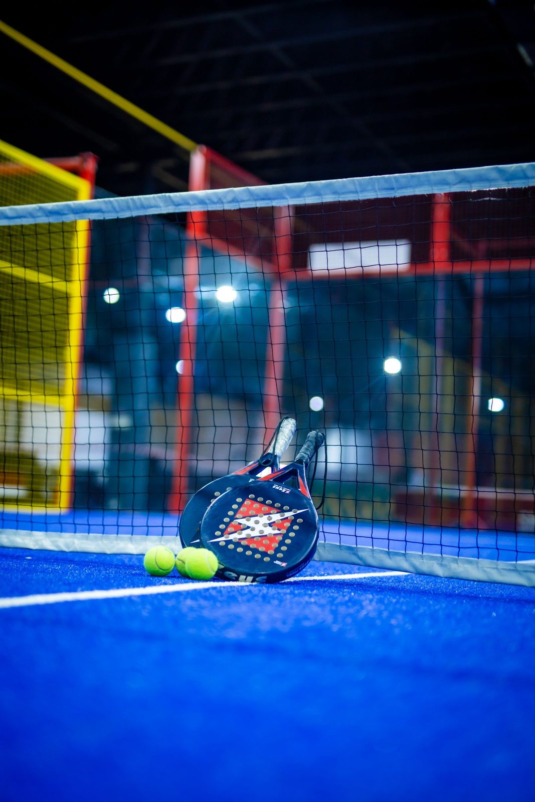 Brightly lit indoor padel court with a racket and balls